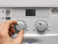 Ręka kręci pokrętłem pieca gazowego dwufunkcyjnego, ustawiając temperaturę. Wyświetlacz pokazuje 49°C.