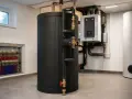 Duży, czarny bufor ciepła z grzałką elektryczną, podłączony do systemu ogrzewania podłogowego.
