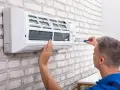 Serwisant naprawia klimatyzator monoblok na białej, ceglanej ścianie.