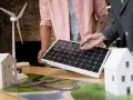 Model domu, panel słoneczny i wiatrak na stole. Dwie osoby omawiają projekt, być może przyszły prosument wirtualny.