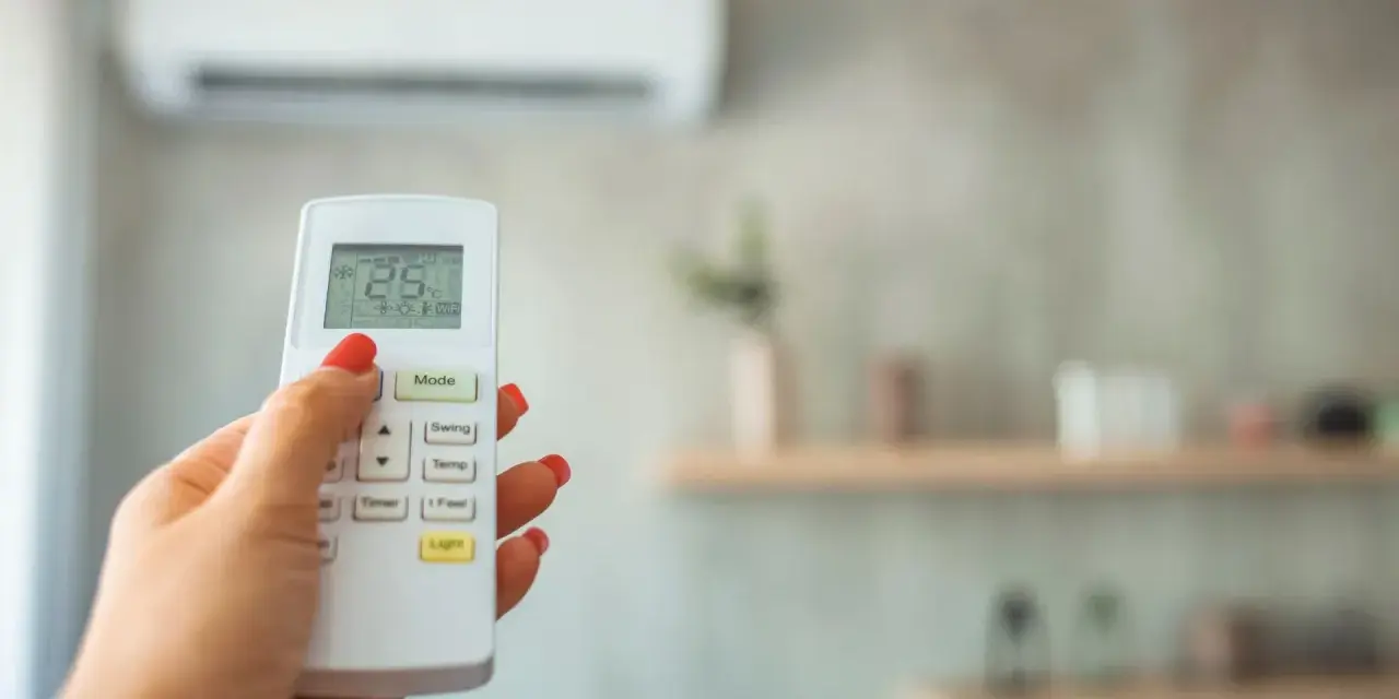 Dłoń z czerwonym lakierem steruje pilotem klimatyzacji, ustawiając 28 stopni. Grzanie klimatyzacją w zimie to komfort.