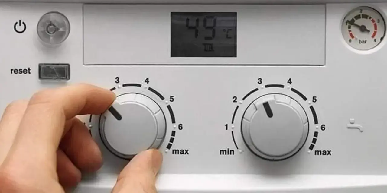 Ręka kręci pokrętłem pieca gazowego dwufunkcyjnego, ustawiając temperaturę. Wyświetlacz pokazuje 49°C.