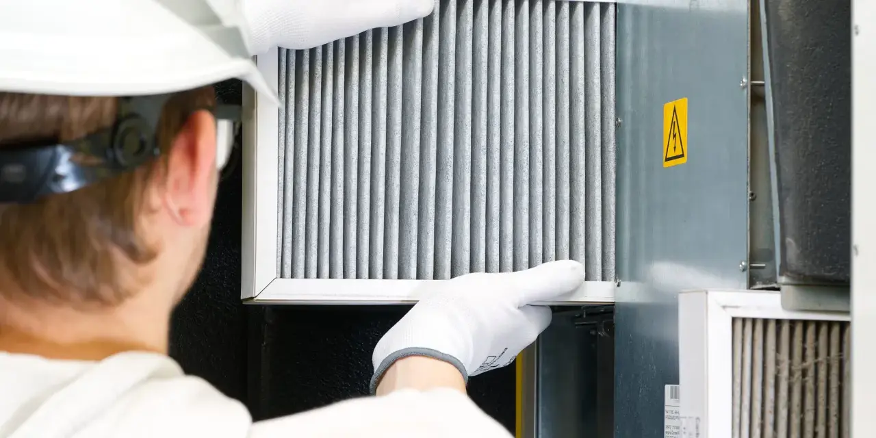 Technik w białej rękawicy wymienia filtr w systemie wentylacyjnym. To ważny element, jak odmulacz do co, zapewniający czyste powietrze.