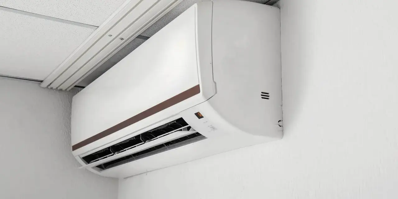 Biała jednostka klimatyzacyjna typu multi split 2 jednostki zamontowana na białej ścianie, pod sufitem podwieszanym.