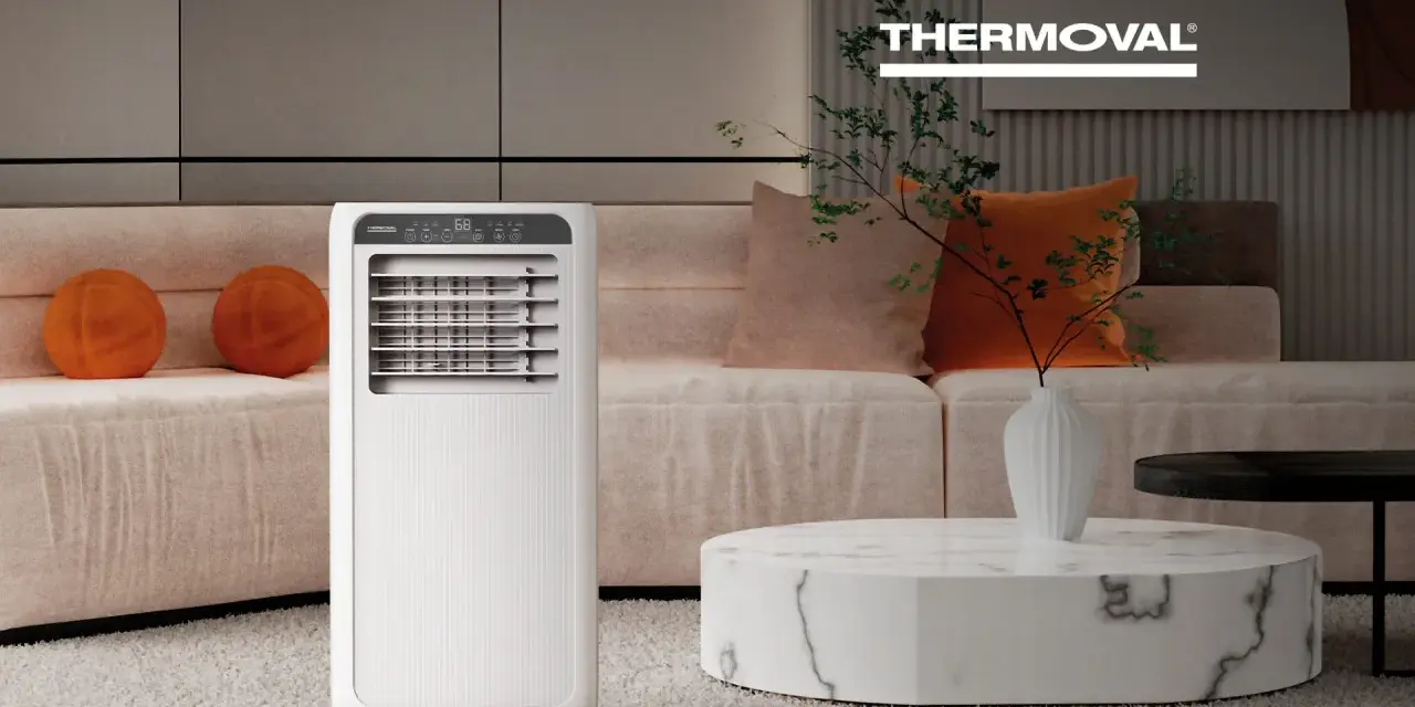 Nowoczesna klimatyzacja w salonie zapewnia komfort. Białe urządzenie Thermoval stoi obok kanapy z pomarańczowymi poduszkami.