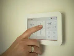 Dłoń dotyka ekranu termostatu, pokazując jak ustawić piec gazowy kondensacyjny ekonomicznie.