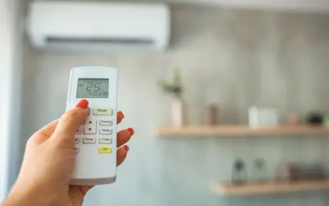 Dłoń z czerwonym lakierem steruje pilotem klimatyzacji, ustawiając 28 stopni. Grzanie klimatyzacją w zimie to komfort.