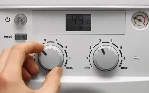 Ręka kręci pokrętłem pieca gazowego dwufunkcyjnego, ustawiając temperaturę. Wyświetlacz pokazuje 49°C.