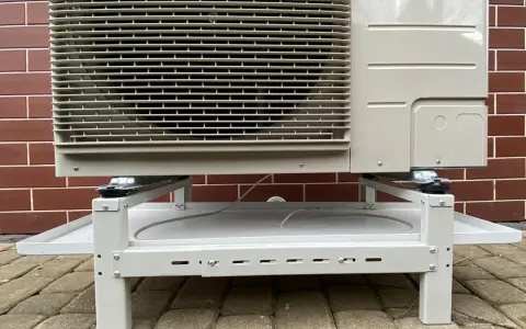 Grzałka tacy ociekowej zapobiega zamarzaniu skroplin. Klimatyzator stoi na metalowym stelażu z tacą.