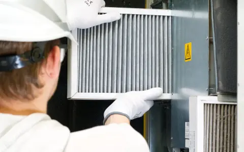 Technik w białej rękawicy wymienia filtr w systemie wentylacyjnym. To ważny element, jak odmulacz do co, zapewniający czyste powietrze.