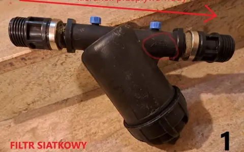 Filtr siatkowy 1 cal, z zaznaczonym kierunkiem przepływu wody.