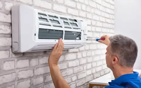 Serwisant naprawia klimatyzator monoblok na białej, ceglanej ścianie.