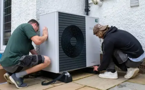 Dwóch mężczyzn instaluje pompę ciepła Bosch 9kW. Urządzenie jest nowoczesne i energooszczędne.