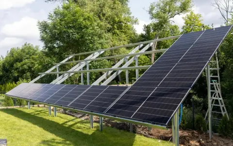 Instalacja fotowoltaiki na gruncie w trakcie budowy. Metalowa konstrukcja i panele słoneczne na trawniku, w tle drzewa. Przepisy dotyczące takich instalacji są kluczowe.