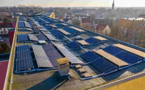 Panele słoneczne na dachu budynku, tworzące instalację, która pozwala na pozyskiwanie energii. To świetny przykład, co to perc-ent energii odnawialnej.