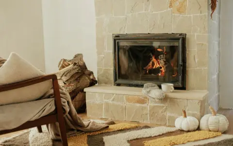 Przytulny salon z palącym się kominkiem, stosem drewna i fotelem. To idealne miejsce, by poczuć ciepło, jakie daje piec akumulacyjny.