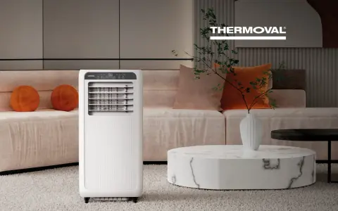 Nowoczesna klimatyzacja w salonie zapewnia komfort. Białe urządzenie Thermoval stoi obok kanapy z pomarańczowymi poduszkami.
