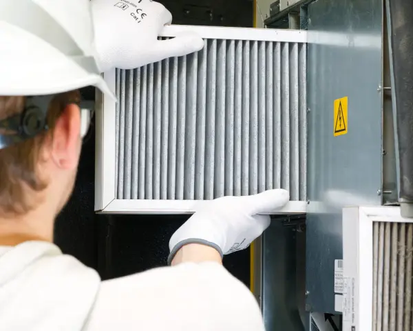 Technik w białej rękawicy wymienia filtr w systemie wentylacyjnym. To ważny element, jak odmulacz do co, zapewniający czyste powietrze.