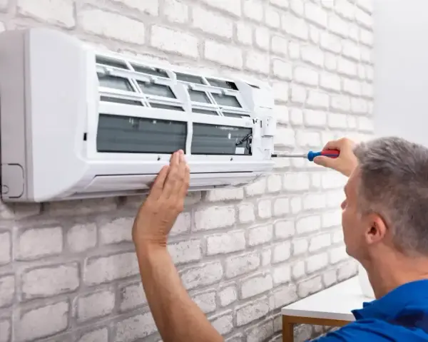 Serwisant naprawia klimatyzator monoblok na białej, ceglanej ścianie.