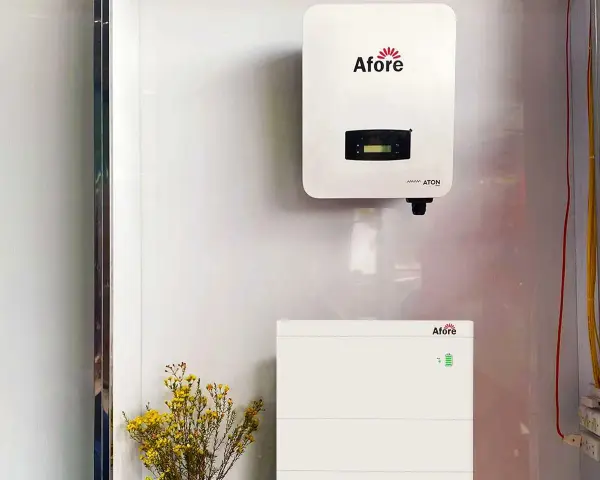 Falownik solis 5kw i jego bateria magazynująca energię, zamontowane na białej ścianie. Obok bukiet żółtych kwiatów.