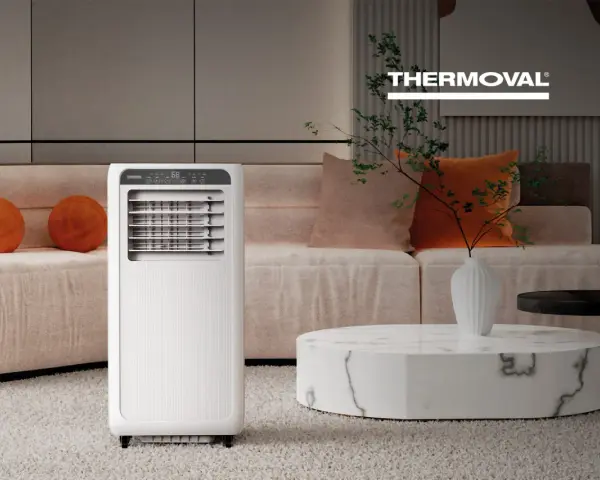 Nowoczesna klimatyzacja w salonie zapewnia komfort. Białe urządzenie Thermoval stoi obok kanapy z pomarańczowymi poduszkami.