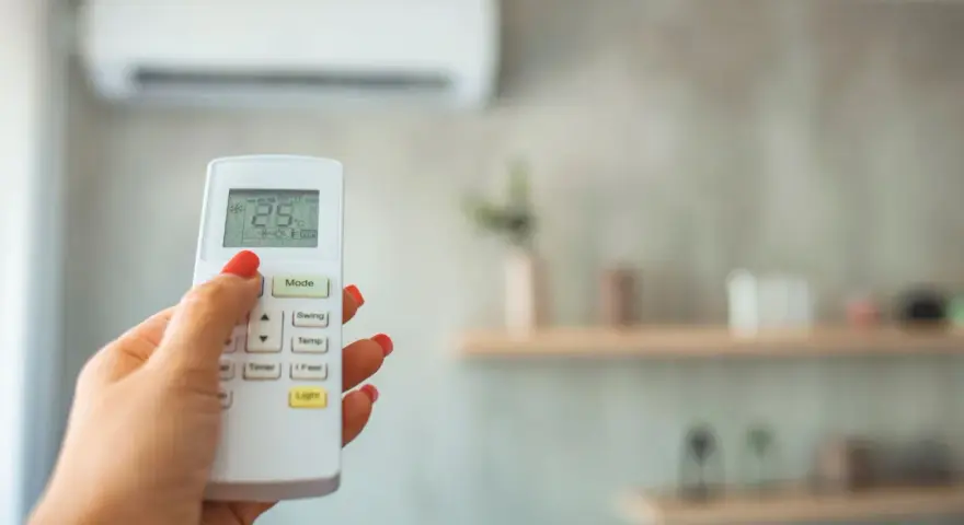 Dłoń z czerwonym lakierem steruje pilotem klimatyzacji, ustawiając 28 stopni. Grzanie klimatyzacją w zimie to komfort.