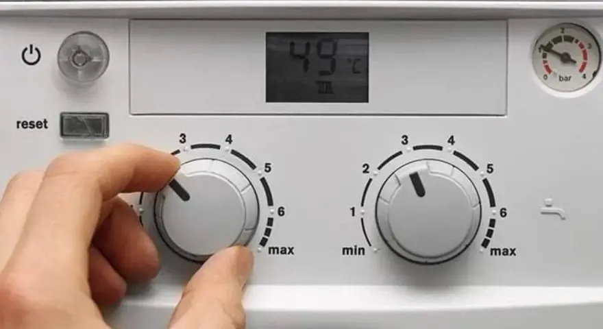 Ręka kręci pokrętłem pieca gazowego dwufunkcyjnego, ustawiając temperaturę. Wyświetlacz pokazuje 49°C.