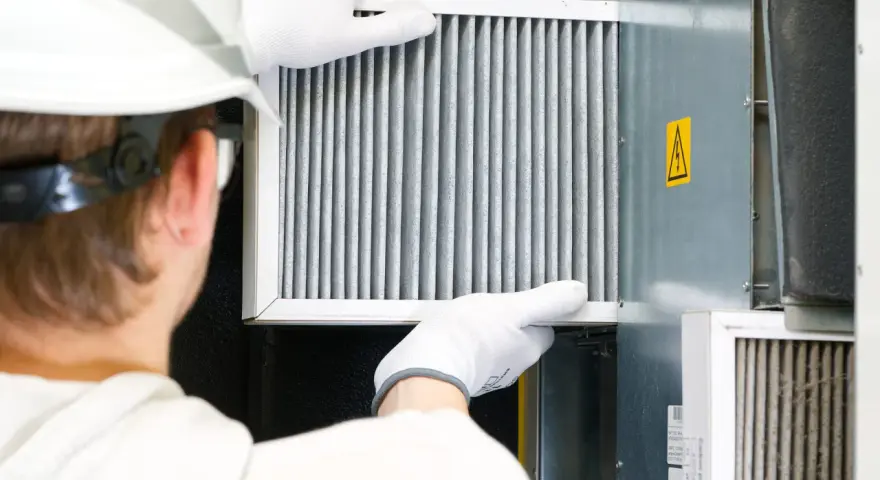 Technik w białej rękawicy wymienia filtr w systemie wentylacyjnym. To ważny element, jak odmulacz do co, zapewniający czyste powietrze.
