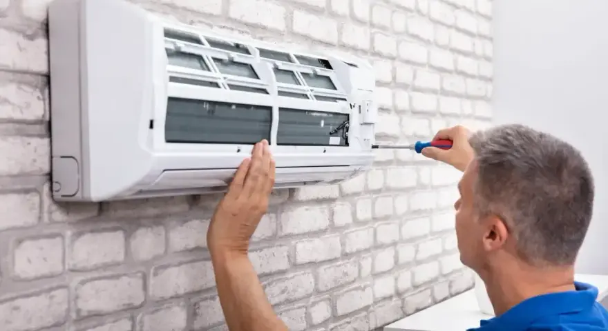 Serwisant naprawia klimatyzator monoblok na białej, ceglanej ścianie.