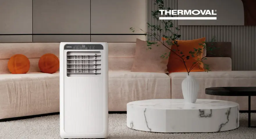Nowoczesna klimatyzacja w salonie zapewnia komfort. Białe urządzenie Thermoval stoi obok kanapy z pomarańczowymi poduszkami.