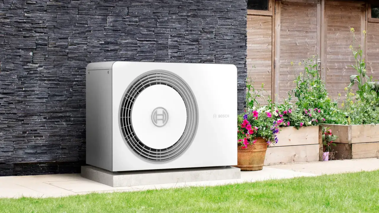 Nowoczesna pompa ciepła Bosch 9kW dyskretnie wkomponowana w otoczenie domu, obok kwitnących kwiatów.
